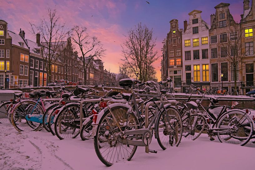 Snowy bikes along the canals in Amsterdam at sunset in the Netherlands in winter by Eye on You