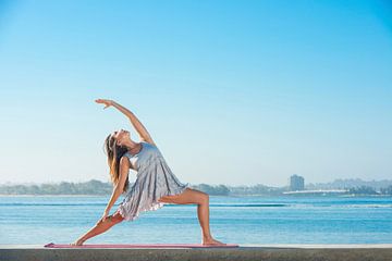 Jonge vrouw in zomerjurk beoefent yoga aan het strand van BeeldigBeeld Food & Lifestyle