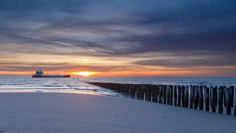 Vrachtschip vaart voorbij aan de kust van Zeeland tijdens zonsondergang. van Menno Schaefer