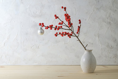 Stechpalmen- oder Ilexzweig mit roten Beeren und einer weißen Weihnachtskugel