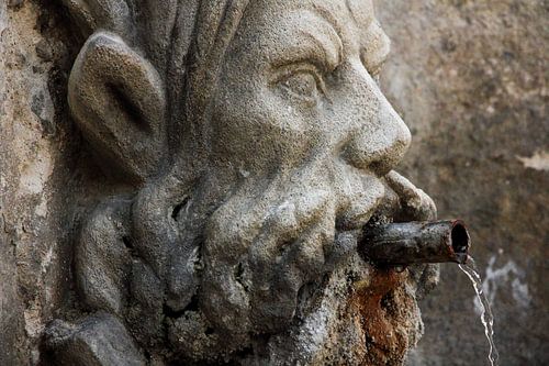 Waterspuwer gebeeldhouwd  uit steen met een koperen pijpje  uit de mond waar water uit komt.