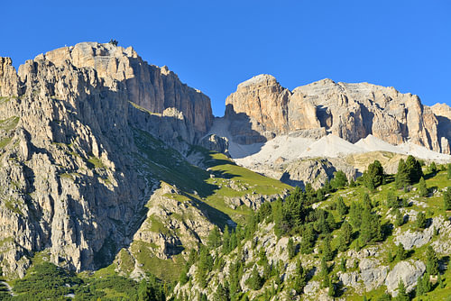 Felsige Berggipfel und steile grüne Hänge unter strahlend blauem Himmel
