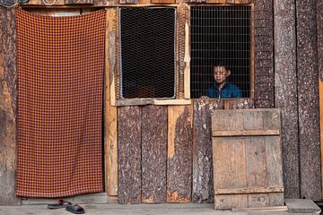 Jongen achter open raam in hut bij Thimphu Bhutan. Wout Kok One2expose van Wout Kok