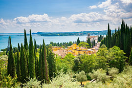 Blick auf ein italienisches Dorf an einem blauen See mit hohen Zypressen und historischen Villen von Menno van der Haven