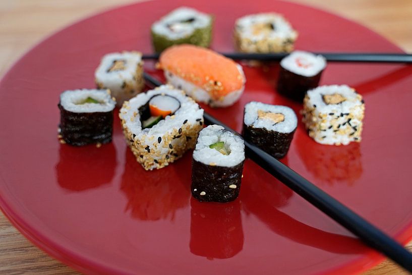 Sushi disposés sur une assiette rouge avec des baguettes. par Babetts Bildergalerie