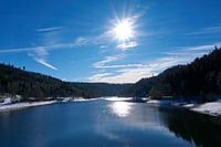 Bevroren rivier met sneeuw en ijs in zonneschijn onder blauwe hemel in Nagoldtalsperre