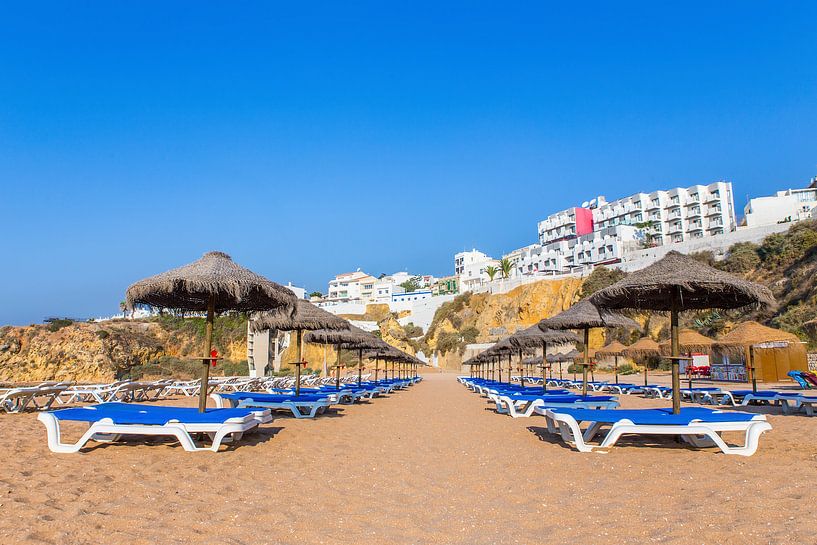 Beach parasols with buildings and blue sky by Ben Schonewille