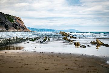 Coastal Beach With Rocky Outcrops and Cliffside Shoreline Under Cloudy Sky