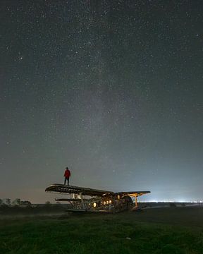 Persoon op verlaten vliegtuig onder sterrenhemel van Ewold Kooistra