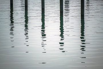 Black mooring piles or dolphins with reflection in the water in  by Maren Winter