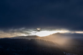 Sonnenlicht durch Wolken und Nebel über einer waldreichen Landschaft von Nanda Bussers