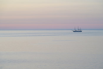 A sailing ship before sunrise during the blue hour on calm waters beneath a pastel-coloured sky