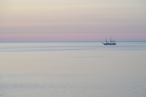 A sailing ship before sunrise during the blue hour on calm waters beneath a pastel-coloured sky