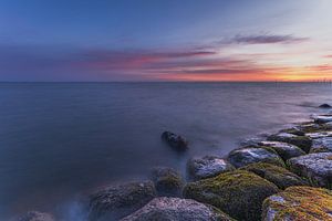 Ein ruhiger Sonnenaufgang über dem Markermeer bei Edam mit moosbewachsenen Steinen und farbenprächtigem Morgenhimmel in Nordholland
