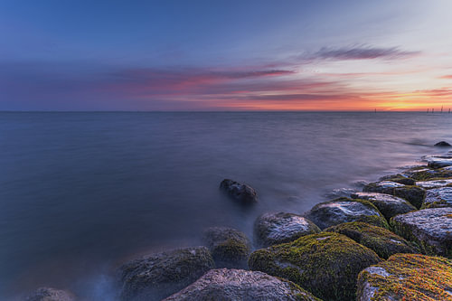 Rustige zonsopkomst boven het Markermeer bij Edam met met mos begroeide stenen en kleurrijke ochtendlucht in Noord-Holland