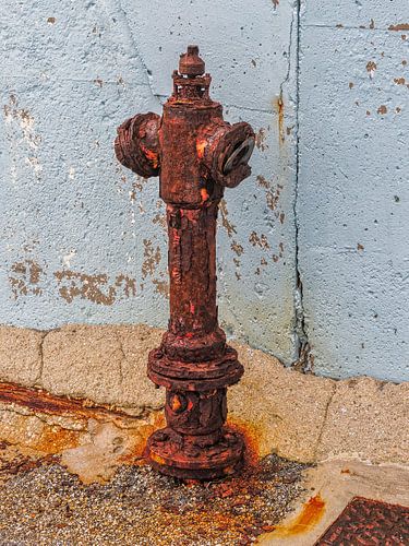 Roestige brandkraan tegen een blauwe muur op Kreta