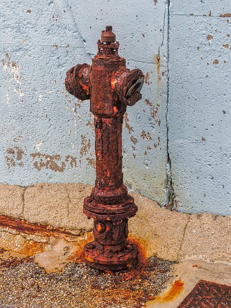 Rusty hydrant against a blue wall in Crete by Luc V. de Zeeuw