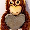 Ein Stoff Affe hängt an einem Herz aus Holz von Tom Voelz