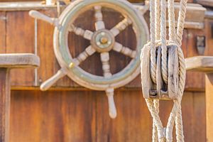 Nautischer Flaschenzug und altes hölzernes Steuerrad auf altem Segelbootdeck von Alex Winter