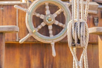 Nautical pulley and vintage wooden helm wheel and on old sailing boat deck by Alex Winter