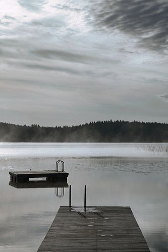 A wooden jetty on the lake in the morning mist, flooded with sunlight and a calm reflection.