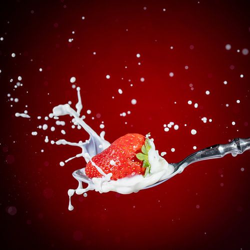 Een lekkere, rijpe, rode aardbei valt op een eetlepel melk