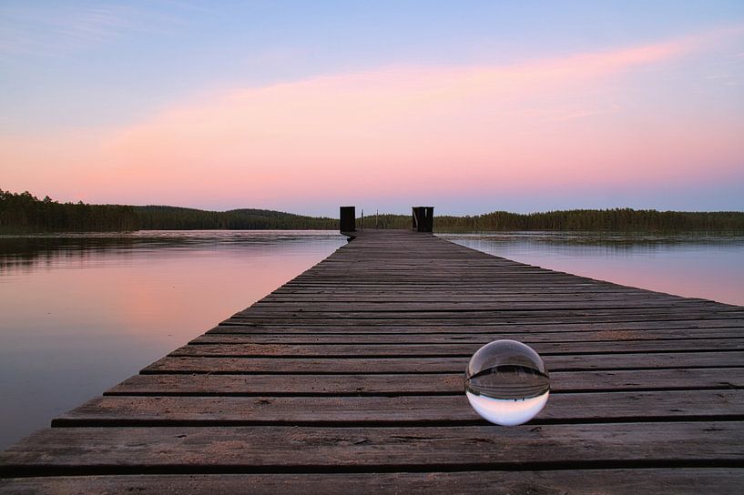 Glass ball on a footbridge reaching into a lake by Martin Köbsch