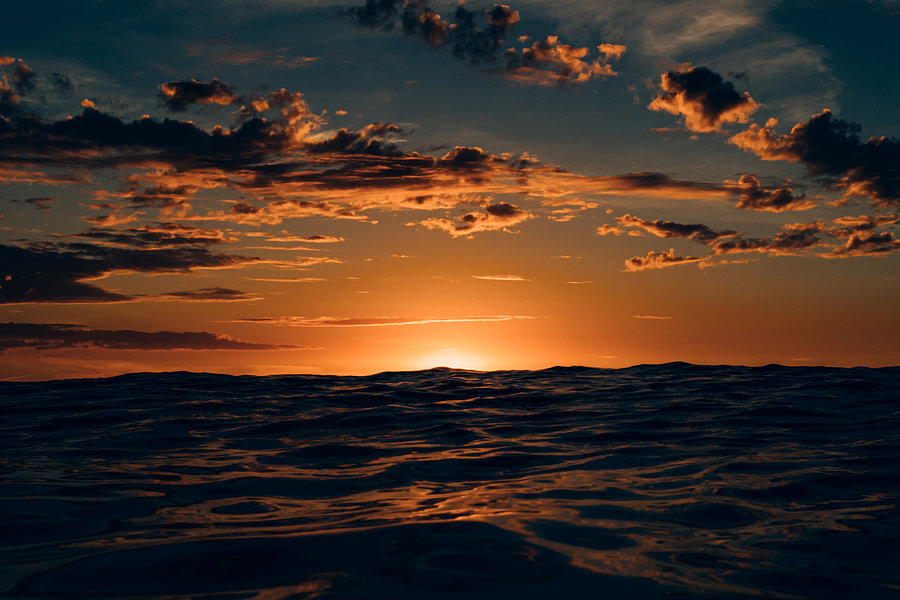 The setting sun hides behind a high wave at the North Sea beach of ...