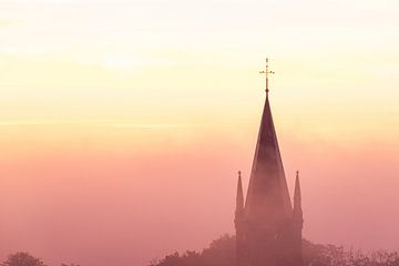 Zonsopkomst tijdens het gouden uur over in een mist gehulde landschap waarbij de kerktoren er boven  van Kim Willems