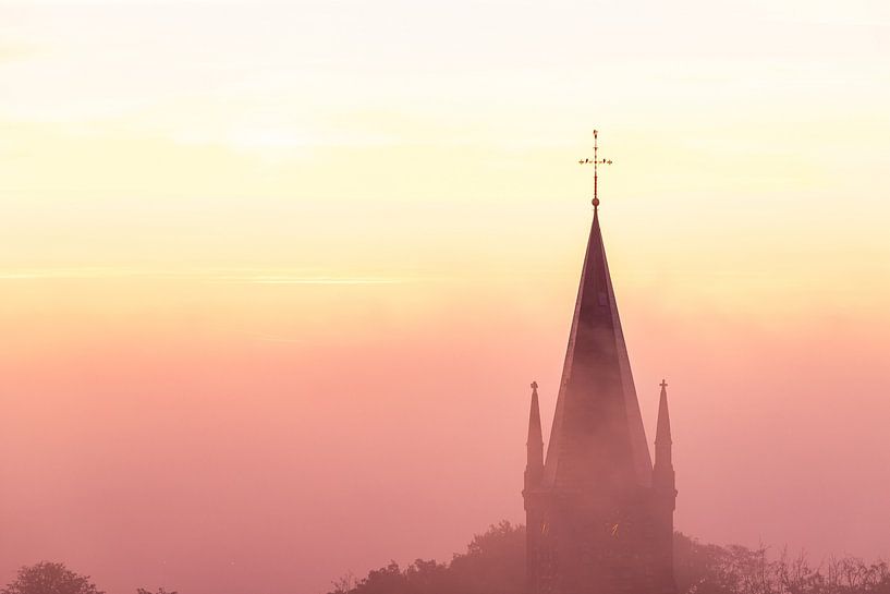 Sunrise during the golden hour over a landscape shrouded in mist, with the church tower rising above by Kim Willems