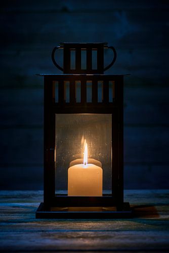 Lantern with burning candle on wooden table in close-up