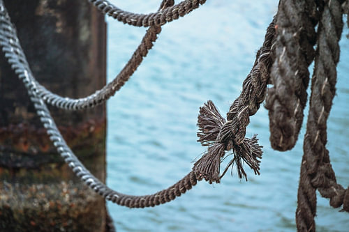 Knoten an einem alten Schiffstau auf einem Steg über dem Wasser, Metapher für