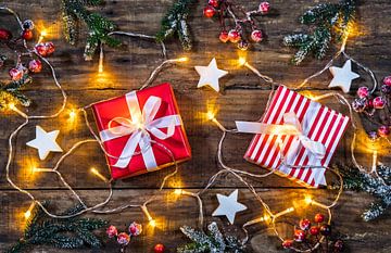 Weihnachtsgeschenke mit Ornamenten, Tannenzweigen, roten Beeren und Licht auf Holz von Alex Winter
