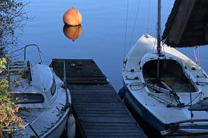 Zwei schmutzige Boote an einer Anlegestelle und eine orangefarbene Boje im blauen, ruhigen Wasser ei