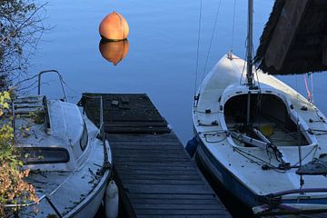 Deux bateaux sales à un quai et une bouée orange dans l'eau bleue et calme d'un lac attendent la fin