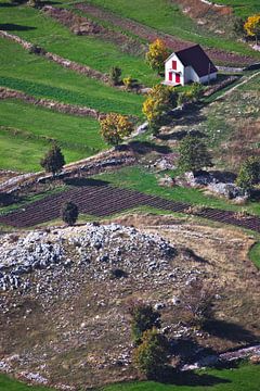 Ein kleines Haus mit einem roten Dach inmitten der smaragdgrünen Alpenwiesen und Steinen weit unten, von Michael Semenov