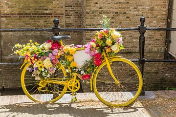 Ein altes gelbes, mit Blumen geschmücktes Fahrrad steht am Zaun einer Gracht in Gouda von Marc Venema