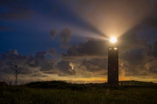 Vuurtoren in de duinen met lichtbundels bij nacht