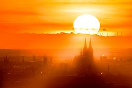 The gaze wanders into the distance, and there, in the midst of the golden veil of the setting sun, Cologne Cathedral rises up. This perspective captures both the vastness of the landscape and the imposing presence of the cathedral. by LICHTERKISTE
