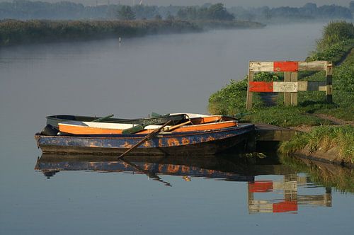 Stilleven met roeiboot in rimpelloos water en hekje op nevelige ochtend in de Duifpolder in Maasland.