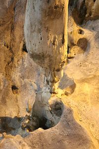 A gnome squats under a stalactite in a dripstone cave.