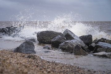 Éclaboussures d'eau de mer avec des rochers et du sable au premier plan sur Margreet Riedstra