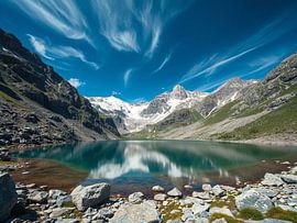 Ein ruhiger Alpensee unter majestätischen schneebedeckten Gipfeln und einem dramatischen Himmel von Artistic