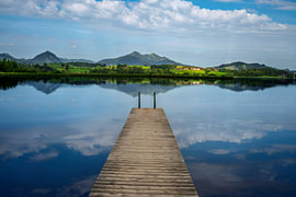 Wooden jetty on Lake Hopfensee beneath a vast cloudy sky by ManfredFotos