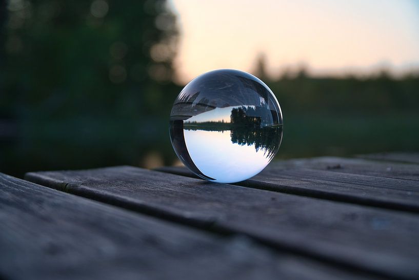 Glass ball on a footbridge reaching into a lake by Martin Köbsch