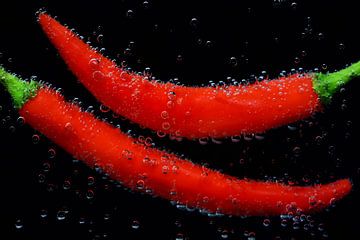Rode paprika's staan onder water met luchtbellen tegen een zwarte achtergrond van Ulrike Leone