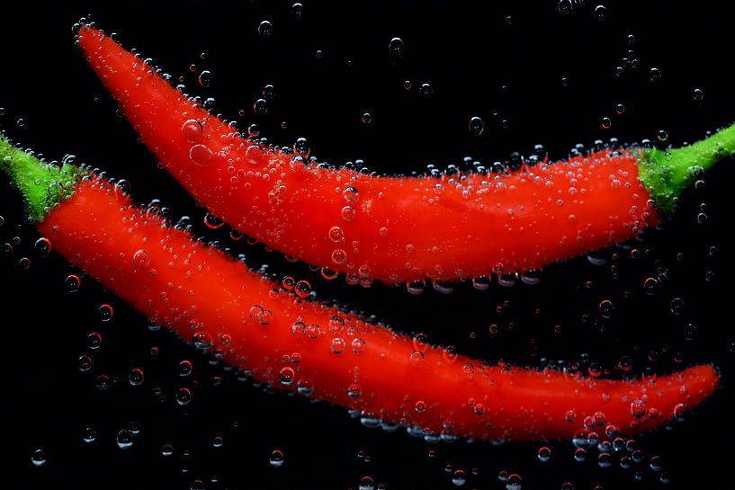 Red peppers are under water with air bubbles against a black background by Ulrike Leone