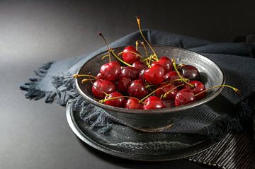 Fresh red cherries in a rustic ceramic bowl with napkin and plate on a dark gray background, healthy by Maren Winter