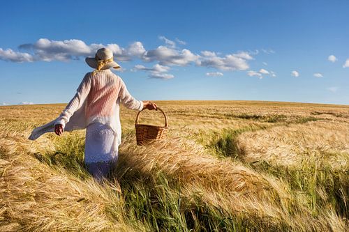 Vrouw met hoed en mand struint door graanveld