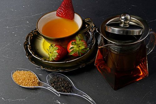 Zwarte thee met aardbei in een kopje en een glazen theepot met theaa
